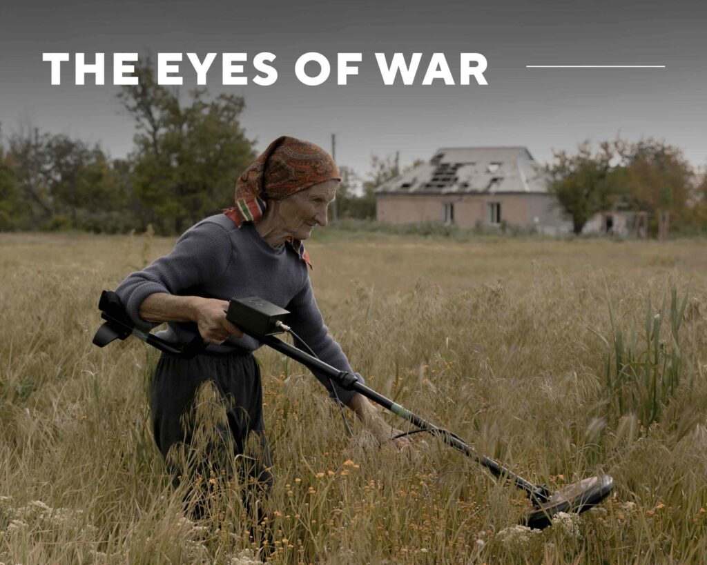 A picture of an elderly woman using a metal detector to scan for mines in a field overlaid with the text "The Eyes of War".